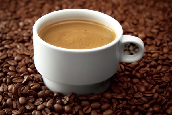 side view of white cup of black coffe on coffee beans. Coffee cream moving in cup